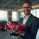 Homme d'affaires confiant tenant une mini Tesla rouge dans un bureau moderne